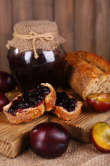 Tasty plum jam in jar and plums on wooden table close-up