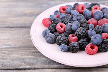 Iced berries on plate, on color wooden background