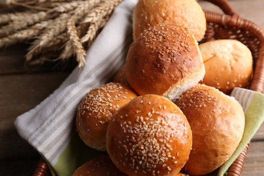 Tasty buns with sesame in wicker basket, on  wooden background