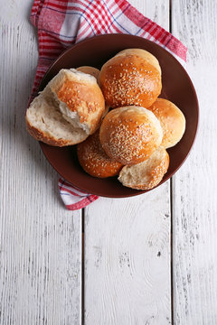 Tasty buns with sesame on plate, on color wooden background