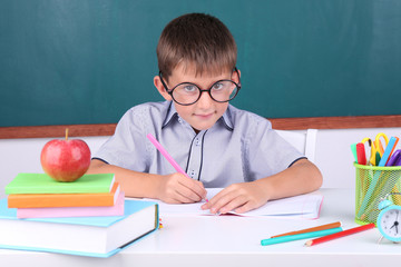 Schoolboy sitting in classroom on blackboard background