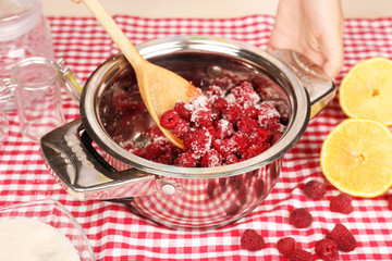 Red raspberries in metal pan, sugar, lemon and glass jars