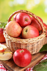 Sweet apples in wicker basket on table on bright background