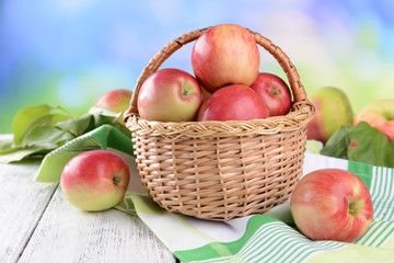 Sweet apples in wicker basket on table on bright background