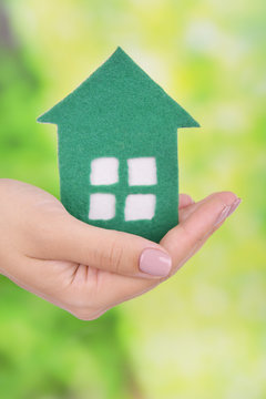 Woman hand holding paper house on bright background