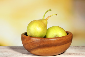Ripe tasty pears in wooden bowl, on table, on nature background