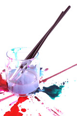Brushes in glass jar with water and spilled paints isolated