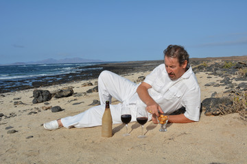 A man with a bottle of wine and two glasses on the beach.
