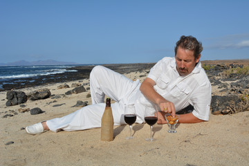 A man with a bottle of wine and two glasses on the beach