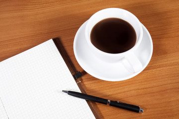 Open a blank white notebook, pen and cup of coffee on the desk
