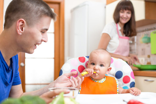 father feeding his baby and mother cooking at kitchen