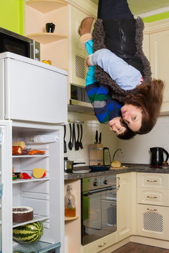 Mother with son stand upside down in kitchen with fridge