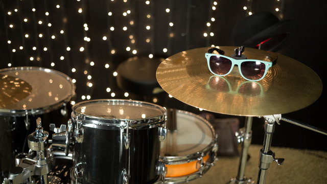Drum set with sunglasses on cymbal in room with garland.