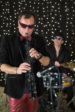 Saxophonist in a bow tie playing saxophone with drumer in club