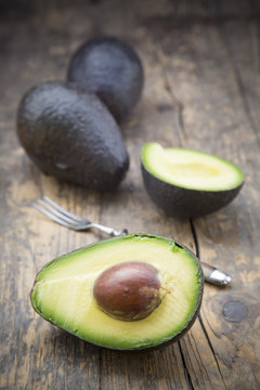 Sliced and whole avocados Persea Americana on wooden table