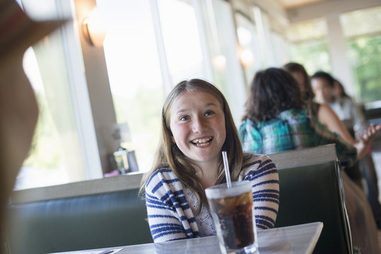 A child seated at a diner with a large cold drink