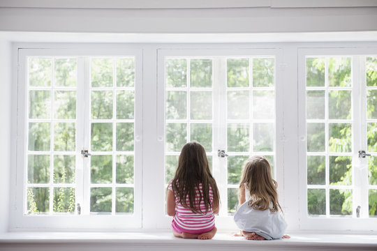 Two girls sitting by large window