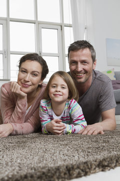 Happy mother, father and daughter lying on carpet in living room