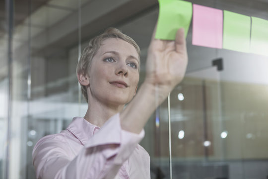Germany, Munich, Businesswoman in office, putting sticky notes on glass pane