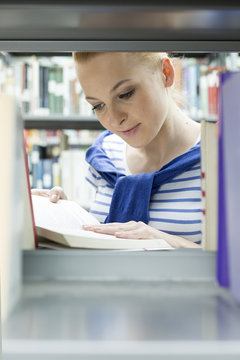 Student in a university library reading book at shelf