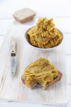 Curry lentils spread made of red lentils, kitchen knife and bitten off slice of bread with curry lentils spread on white wooden board
