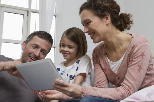 Mother, father and daughter on couch with tablet computer