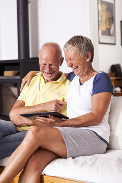 Senior couple sitting on couch having fun with digital tablet