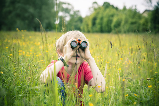 Little boy sitting on meadow watching something with binocular