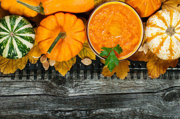 Pumpkin cream-soup and pumpkins on the wooden background