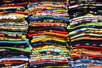 magliette di cotone impilate l'una sull'altra pronte per essere vendute ai turisti. Ottima fattura, colori brillanti e vivaci per prodotti per vestire bambini, adulti e anche anziani - obrazy, fototapety, plakaty