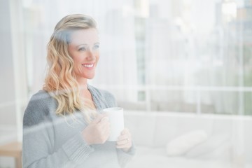 Smiling blonde woman holding mug of coffee looking away