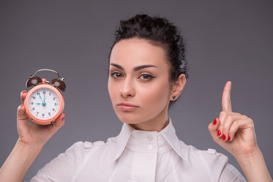 Portrait of pretty girl holding an alarm clock in her hand showi