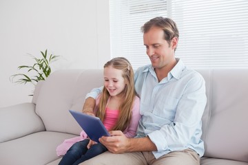 Casual father and daughter using tablet on the couch