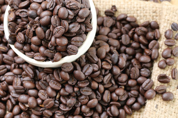 Coffee beans placed on bag sack and white cup.
