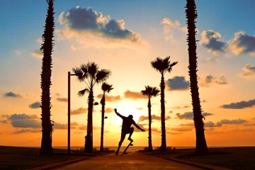 Rolgordijnen man jumping on skateboard near the ocean in sunset © Alex from the Rock