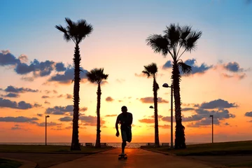 Rolgordijnen man riding on skateboard near the ocean in sunset © Alex from the Rock