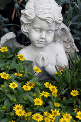 Fototapeta premium little praying angelic figure among the growing flowers on tomb