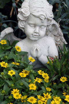 little praying angelic figure among the growing flowers on tomb