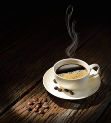 Cup of coffee with smoke and coffee beans on old wooden table
