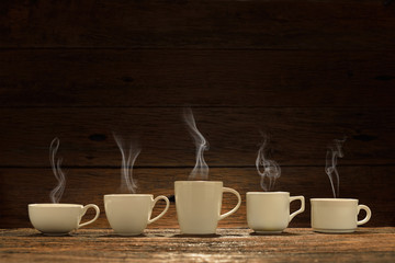 Variety of cups of coffee with smoke on wooden background