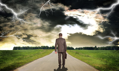 Businessman with briefcase walking on road ahead. Rear view