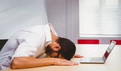 Casual businessman feeling exhausted at his desk