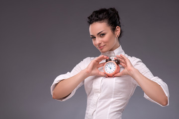 Portrait of pretty girl holding an alarm clock in her hand showi
