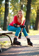 Beautiful young woman in roller skates sitting on park bench