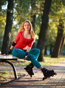 Beautiful young woman in roller skates sitting on park bench