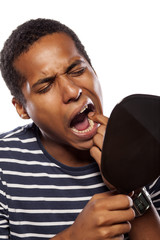 dark-skinned young man looking at his teeth in the mirror