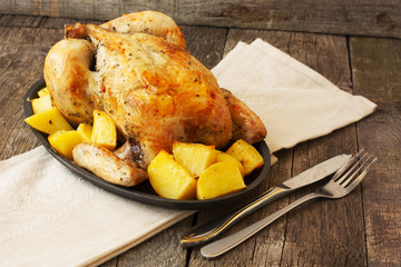 chicken baked with potatoes on a cast iron pan on a wooden backg