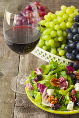 a glass of wine and salad with grapes, herbs, walnuts and blue c