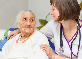 young nurse caregiving an old lady lying in bed