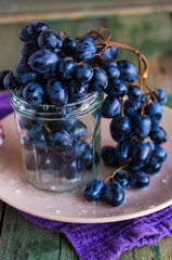 twig branch of blue grapes in a glass on a plate, raw food